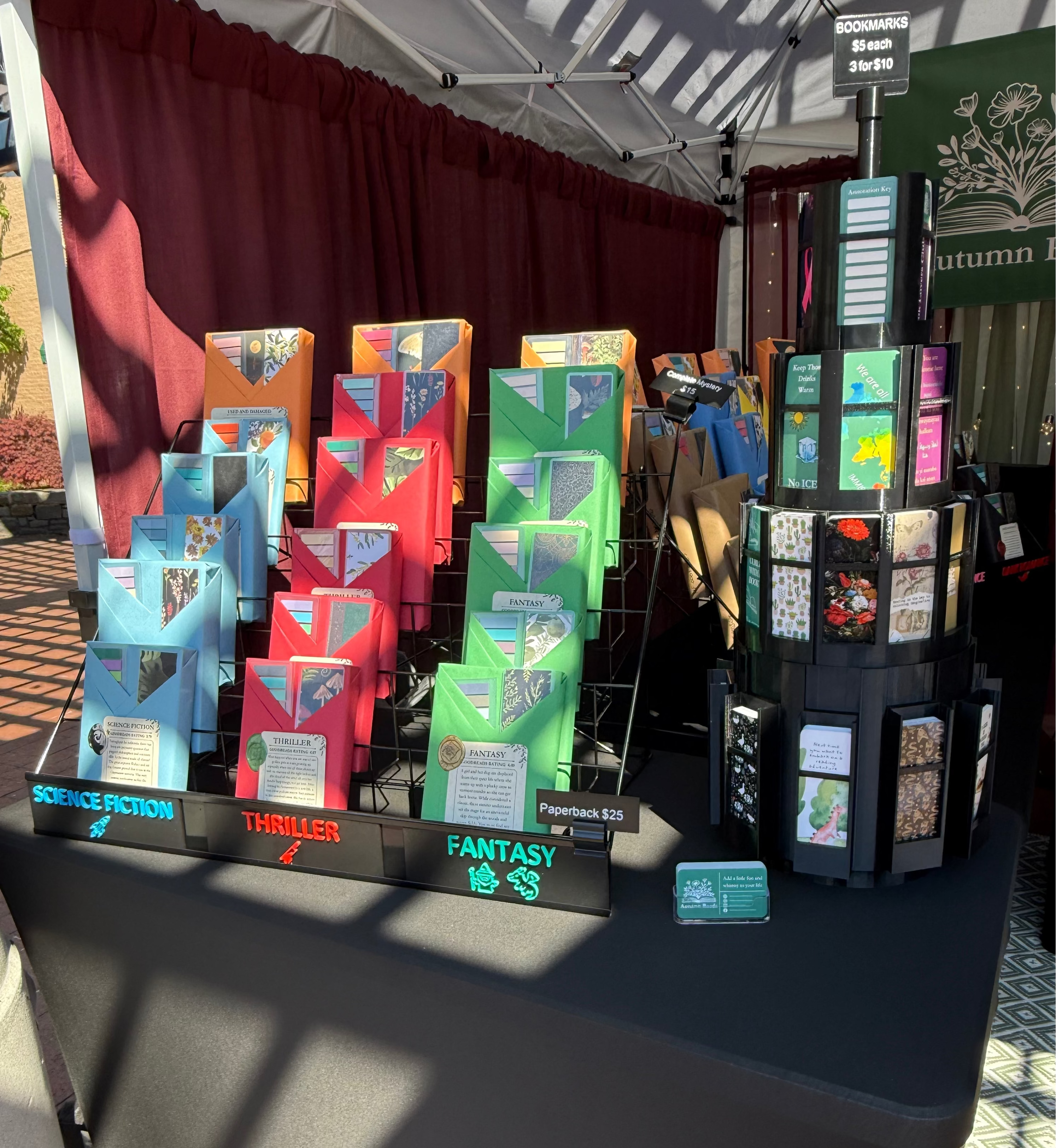 Display of books categorized by genre on a table outdoors.
